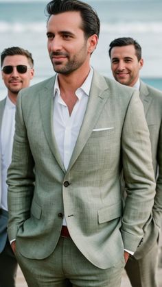 a man in a suit and sunglasses standing on the beach with other men behind him