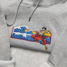 the hoodie is embroidered with an image of a man on a surfboard and waves