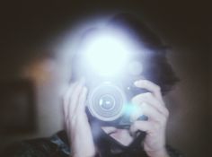 a person holding a camera up to their face in front of a mirror with the light on