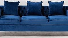 a blue couch with four pillows on it in front of a white wall and floor