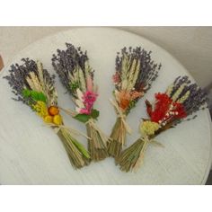 four dried flowers sitting on top of a white plate next to a person's hand