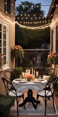 an outdoor dining area with candles and flowers on the table, surrounded by potted plants