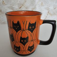 an orange coffee mug with black cats and pumpkins painted on the inside is sitting on a table