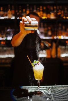 a bartender sprinkles the top of a cocktail in front of an empty bar