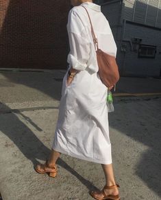 a woman walking down the street with a handbag on her shoulder and wearing sandals