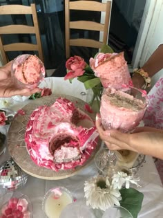 three people are holding up pink frosted cakes on a table with flowers and candles