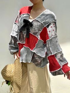 a woman wearing a red and grey sweater holding a straw hat in her hand while standing next to a white wall