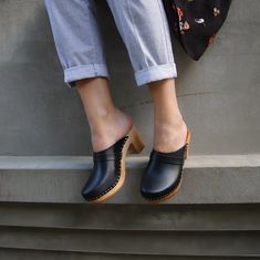 a woman's feet wearing black clogs standing on the edge of a step