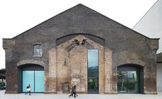 two people walking in front of an old brick building with glass doors and arched doorways