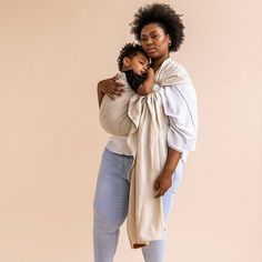 a woman holding a baby in her arms while standing next to a wall and looking at the camera