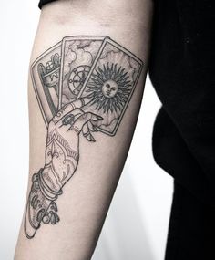 a person with a tattoo on their arm holding two playing cards