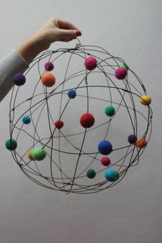 a person is holding a metal ball with multicolored balls on it and their hands are reaching for the ball