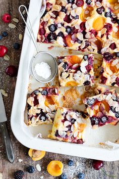 a white tray topped with fruit cobbler next to a knife and bowl of berries