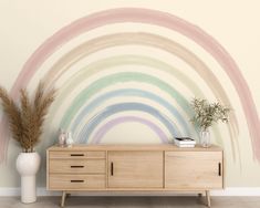 a white vase sitting on top of a wooden dresser next to a wall with a rainbow painted mural