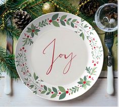 a plate with the word joy painted on it next to pine cones and christmas decorations