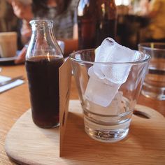 a wooden table topped with two glasses filled with liquid and ice cubes next to each other