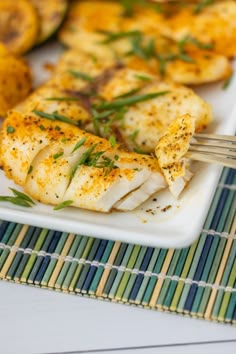 a white plate topped with fish next to potatoes and green garnish on a bamboo mat