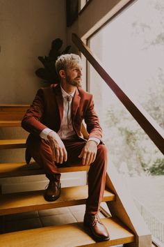 a man in a suit sitting on some stairs looking out the window with his feet propped up