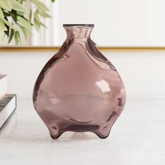 a pink vase sitting on top of a white table next to a book and plant