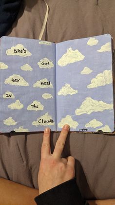 a hand is pointing at an open book with clouds on it and she's got her in the clouds