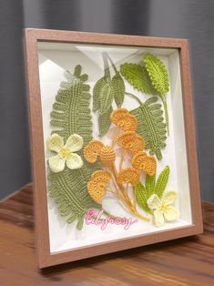 a wooden frame with crocheted flowers and leaves