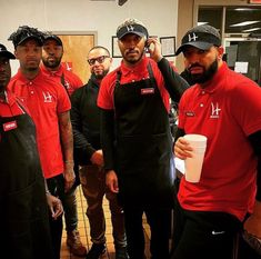 men in red shirts and black aprons are posing for the camera with one man holding a coffee cup