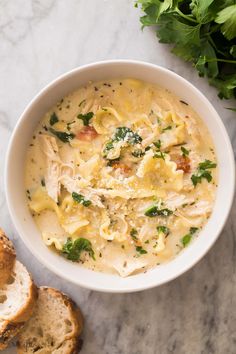 a white bowl filled with chicken noodle soup next to slices of bread and parsley