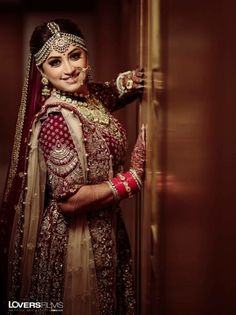 a woman in a red and gold bridal outfit standing next to a door with her hands on her hips