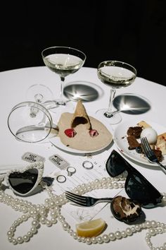 a white table topped with plates and glasses filled with desserts next to wine glasses