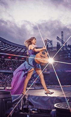 a woman in a purple dress is playing the guitar on stage at a sporting event