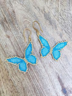 two blue butterfly earrings sitting on top of a wooden table