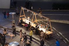 a group of people standing around tables on a wooden deck with lights and umbrellas