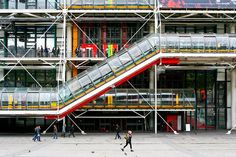 people are walking around in front of a building with an escalator and stairs