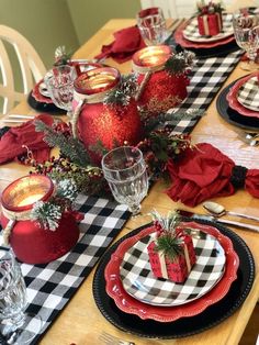 the table is set for christmas dinner with red and black plates, plaid napkins, silverware and candlesticks