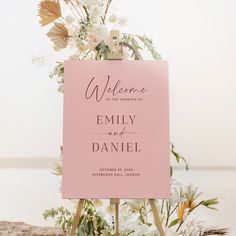 a pink welcome sign sitting on top of a wooden easer next to white flowers