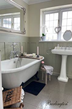 a white bath tub sitting next to a sink in a bathroom under a mirror with candles on it