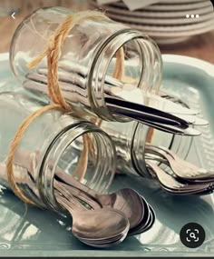 two glass jars with spoons and forks tied to each other on a blue plate