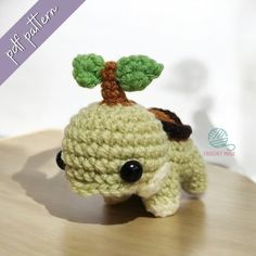 a small crocheted stuffed animal with a tree on it's head sitting on top of a wooden table