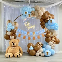 a teddy bear sits in front of a balloon arch for a baby's first birthday