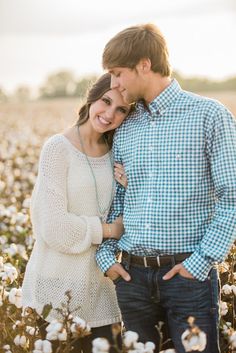 a man and woman standing in the middle of a field with cotton flowers at sunset