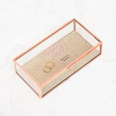 a pink and gold jewelry box with two wedding rings on the inside that says happily