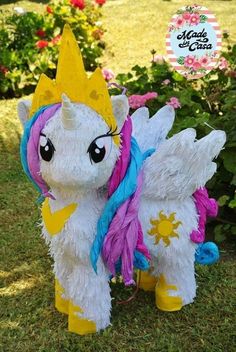 a white and pink pony with wings standing in the grass next to some flowers on a sunny day