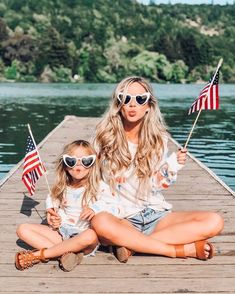 two women sitting on a dock holding american flags