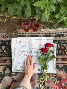 someone is writing on a newspaper with two glasses next to it and roses in the foreground