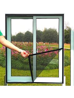 a person is opening the side of a glass door to look out onto a flower garden