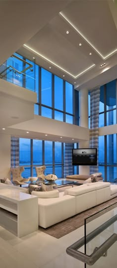 a living room filled with white furniture and large windows overlooking the ocean at night time