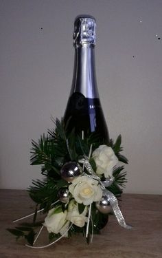 a bottle of champagne with white flowers and greenery on the table next to it