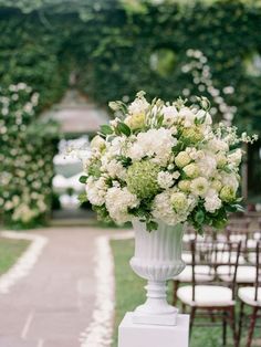 a vase filled with white flowers sitting on top of a lush green field next to rows of chairs