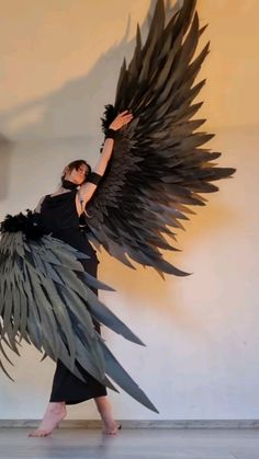 a woman is dressed in black and has large wings on her back, as she holds onto the wing of an object