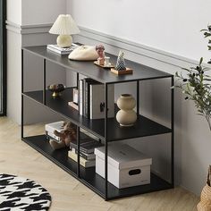 a black shelf with books and vases on it in front of a white wall